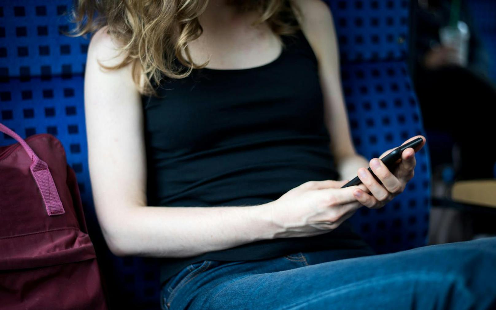 Eine Frau sitzt in einem Zug der Deutschen Bahn und sieht auf ihr Smartphone. Symbolfoto.