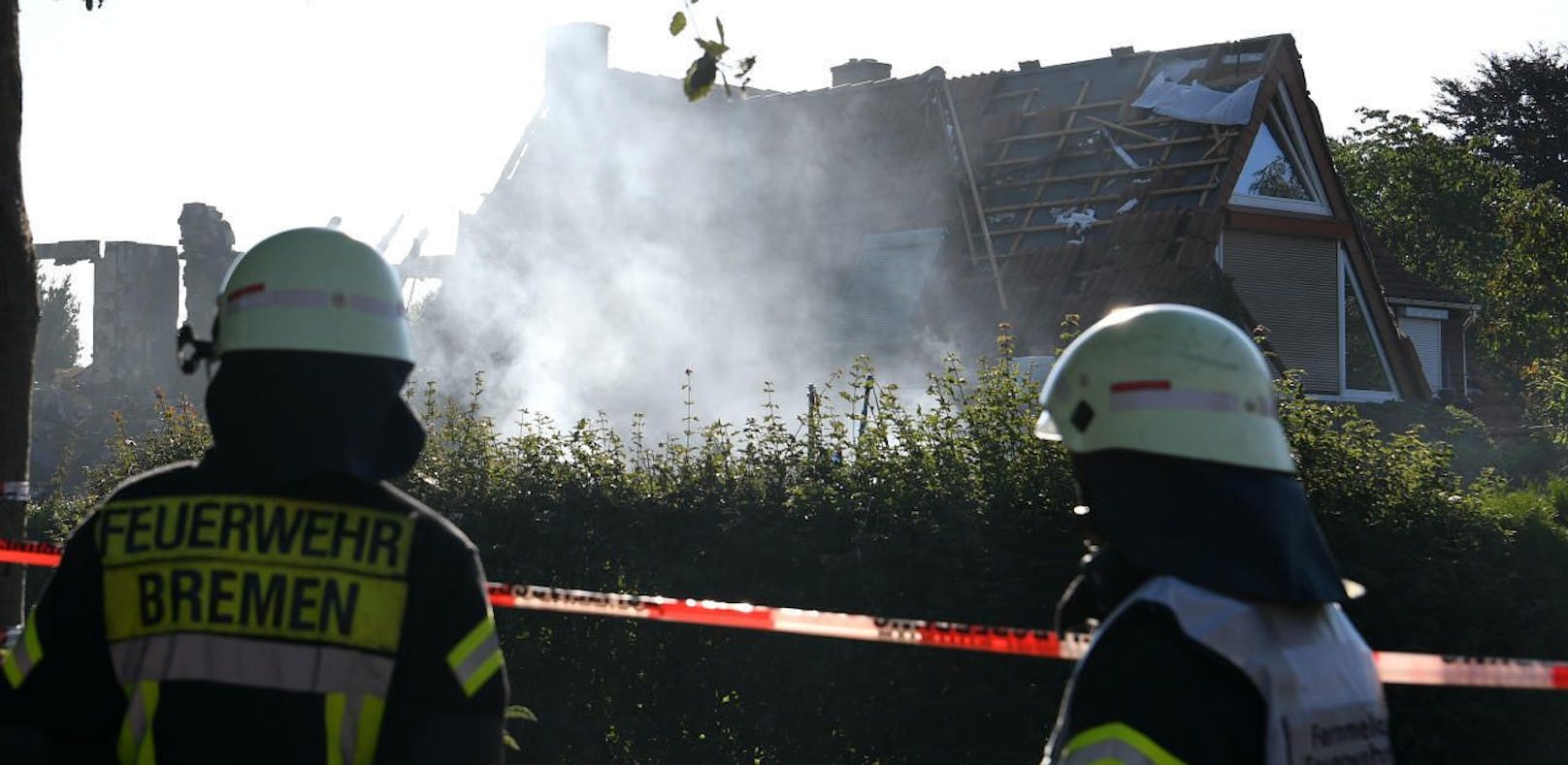 Feuerwehrmänner schauen auf das noch rauchende Wohnhaus, das bei einer Explosion zerstört wurde.