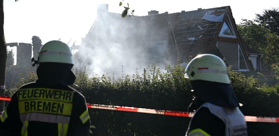 Feuerwehrmänner schauen auf das noch rauchende Wohnhaus, das bei einer Explosion zerstört wurde.