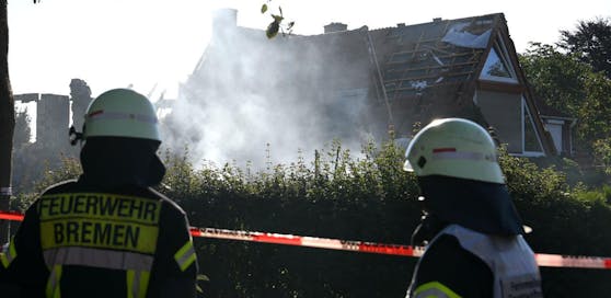 Feuerwehrmänner schauen auf das noch rauchende Wohnhaus, das bei einer Explosion zerstört wurde.
