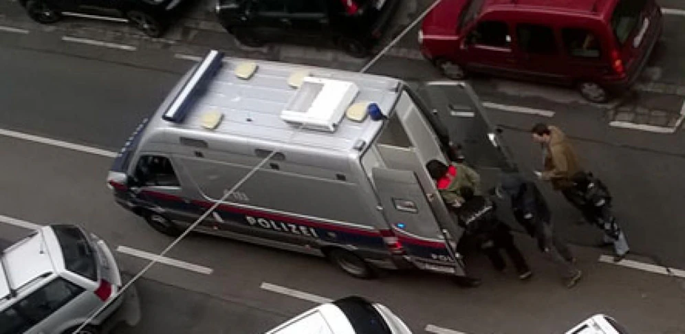 Polizei-Beamte bringen Verdächtige in den Arrestwagen.