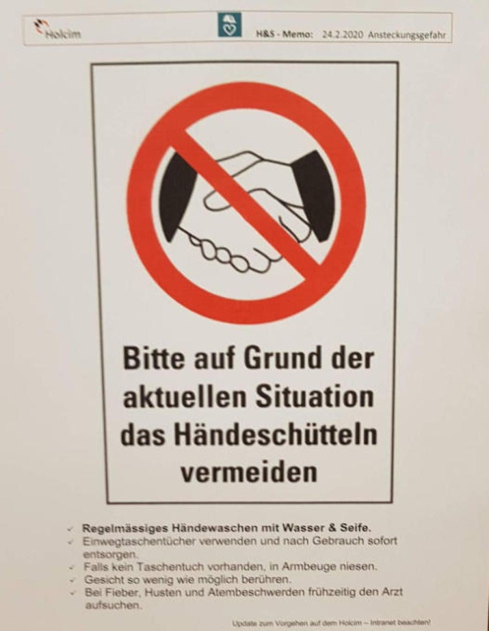 "Bitte auf Grund der aktuellen Situation das Händeschütteln vermeiden" heißt es auf einem Flyer, der vor dem Eingang zur Kantine des Holcim-Zementwerks in Untervaz (Schweiz) hängt. Darauf zu sehen: zwei Hände beim Handshake, darüber ein rotes Verbotszeichen.