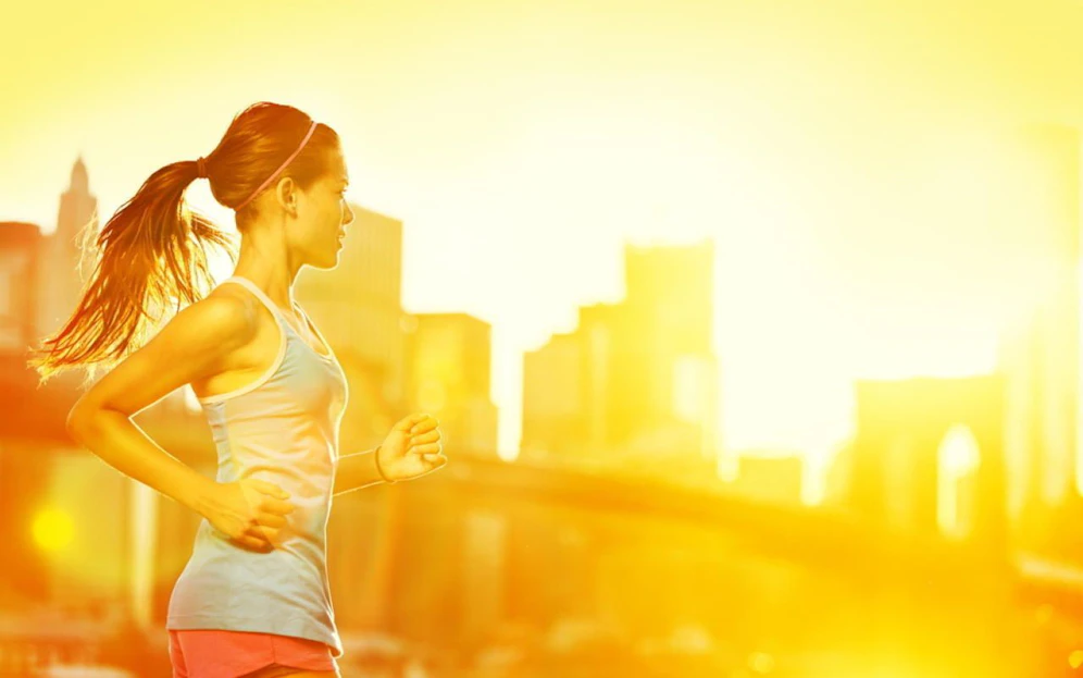 Running woman. Runner jogging in sunny bright light. Female fitness model training outside in New York City with skyline and Brooklyn Bridge in background.