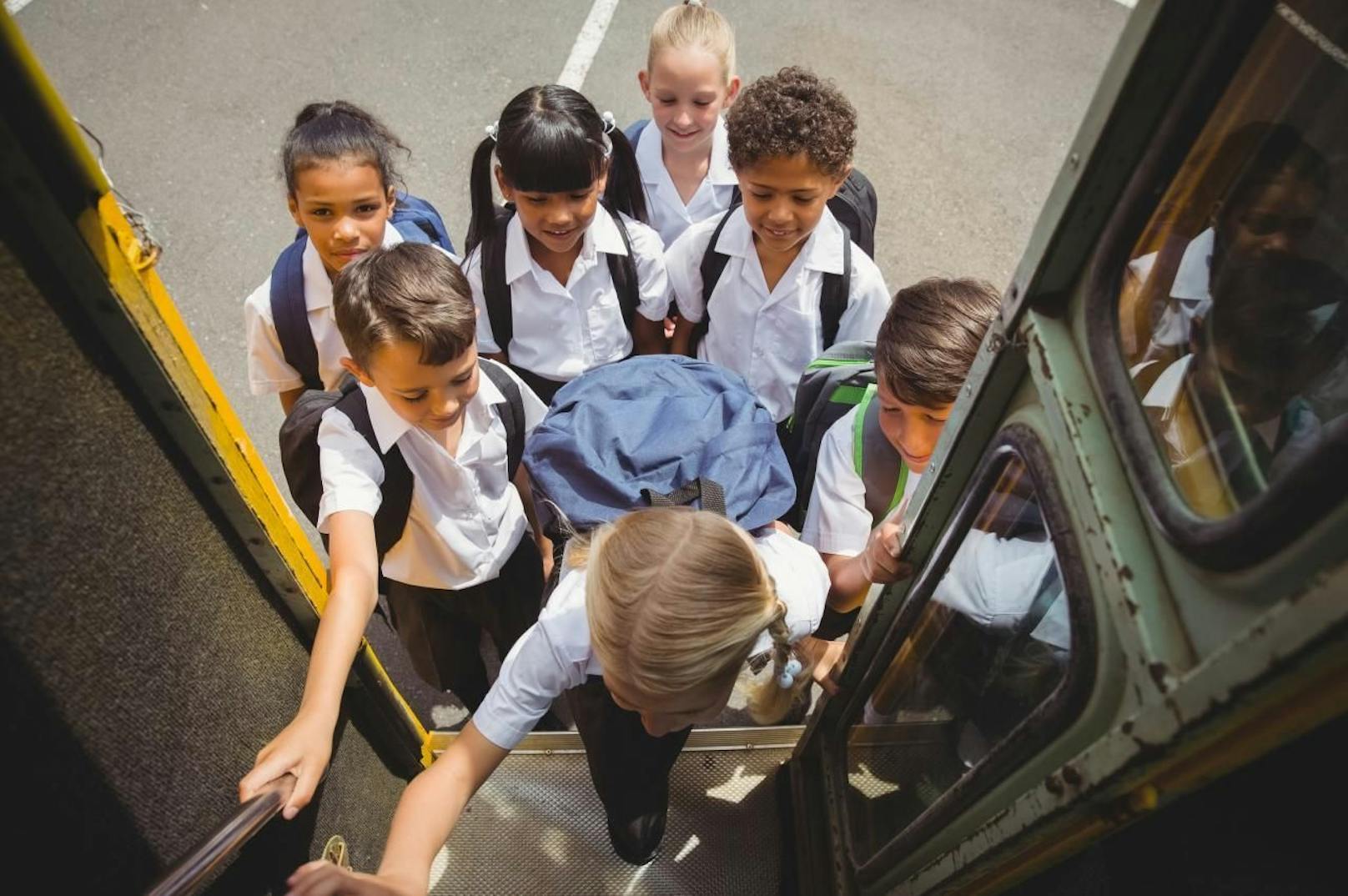 Mädchen und Buben beim Einsteigen in einen Schulbus.