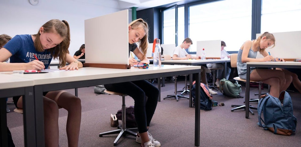 Symbolbild: Schüler schreiben eine Prüfung mit Sichtschutz zum Sitznachbarn.