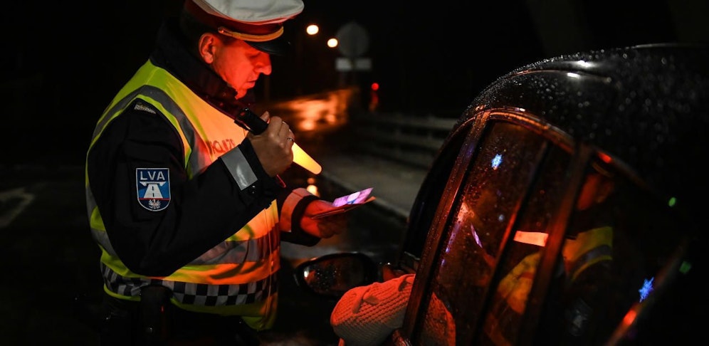 Ein Polizist bei einer Personen- und Fahrzeugkontrolle mit Rotlicht.