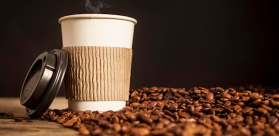 Ein Kaffeebecher vor gerösteten Bohnen. Symbol