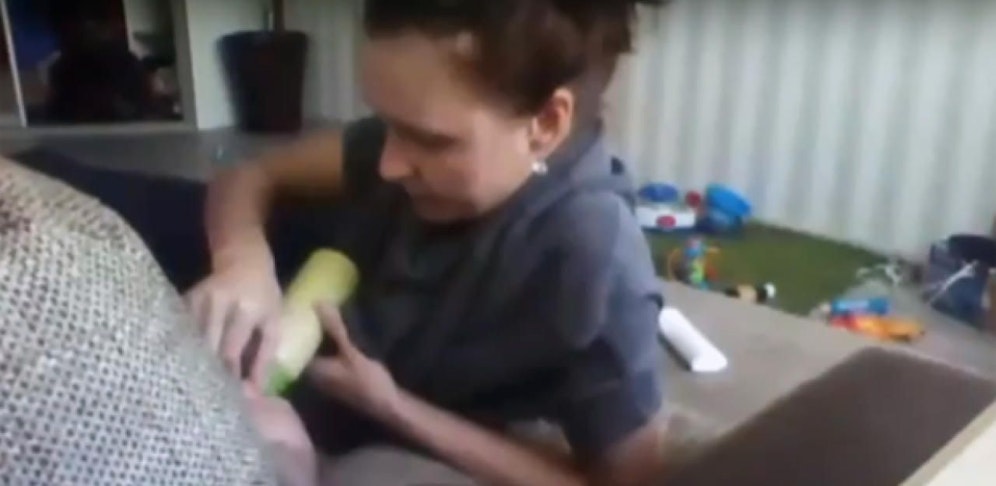 Die Frau hält dem Buben die Nase zu, damit er sein Fläschchen trinkt.