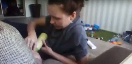 Die Frau hält dem Buben die Nase zu, damit er sein Fläschchen trinkt.