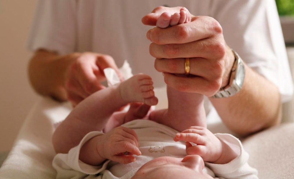 Ein Mann wechselt die Windeln eines Babys. Symbolfoto