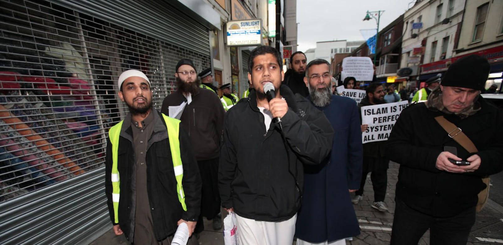 Siddhartha Dhar aka Abu Rumasayah, (in der Mitte mit Mikro)  bei Protesten in London 2013.