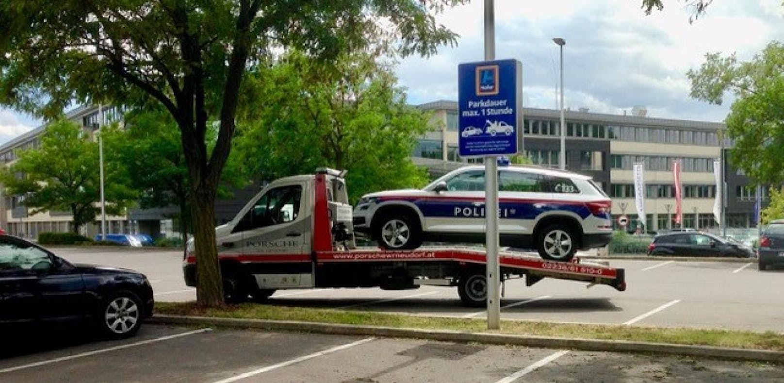 Abschlepp-Auto nimmt Polizeiwagen auf die Schaufel, davor warnt ein Schild vor Falschparken