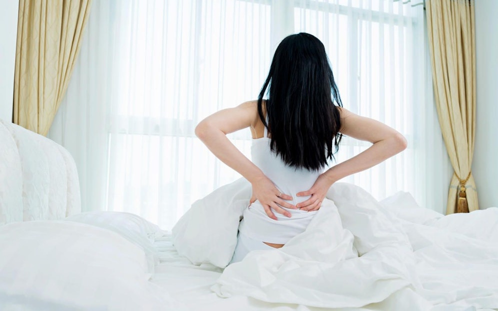 Young lady waking up and sitting in bed with hands raised. Rückenschmerzen
