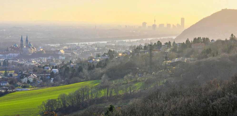 Blick an einem dunstigen Nebeltag im Dezember von den Abhängen des Wienerwald über landwirtschaftlich genutzte Wiesen und Felder und den Ort Klosterneuburg vorbei am Leopoldsberg zum UNO City Wien oder Vienna International Centre und weiter zu den Wiener Bezirken nördlich der Donau.