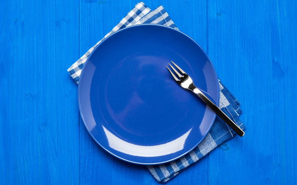 Blue plate with fork on napkin and blue table