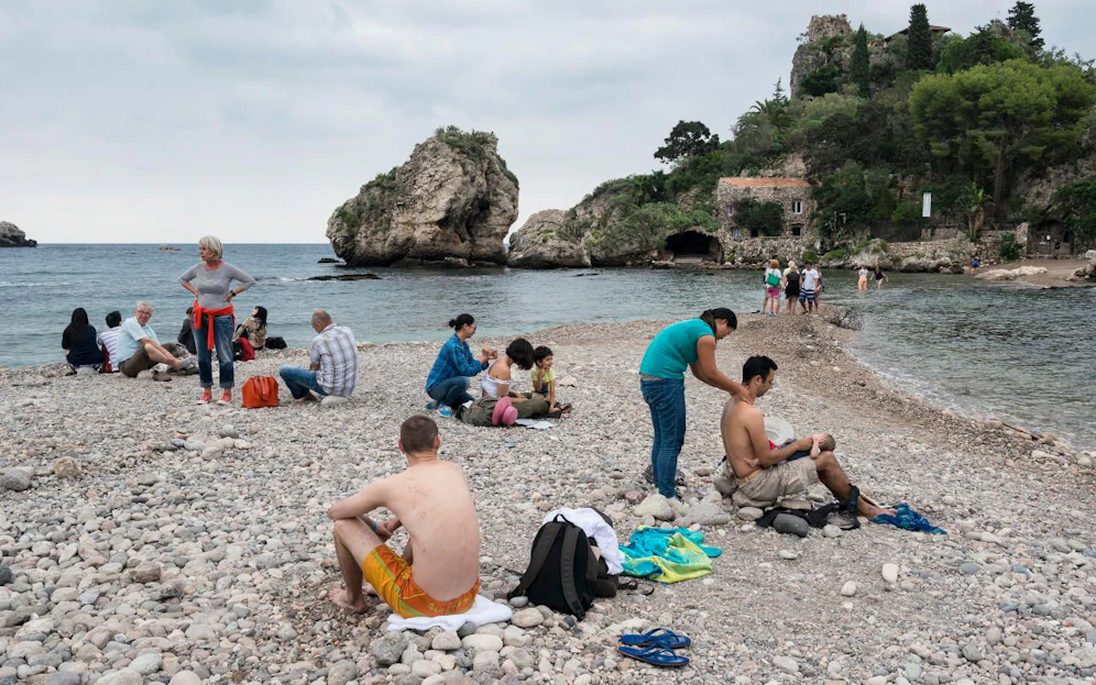 Eine Frau massiert Touristen am Strand von Taormina, Italien.