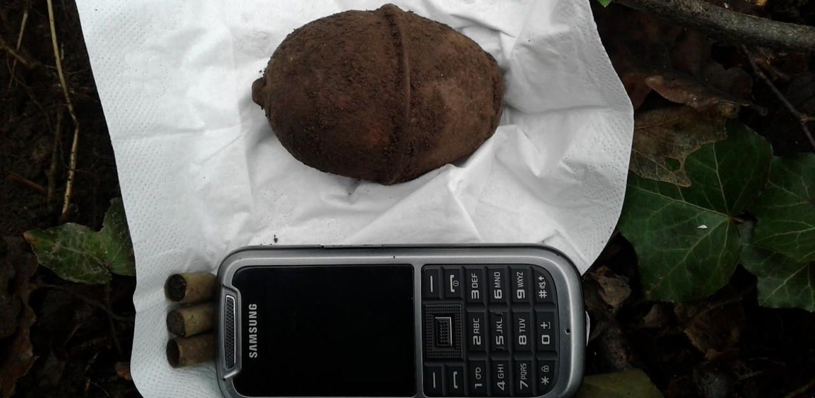 Ein Spaziergänger fand diese  Eierhandgranate. Zum Größenvergleich legte die Polizei ein Mobiltelefon neben den Fund. 