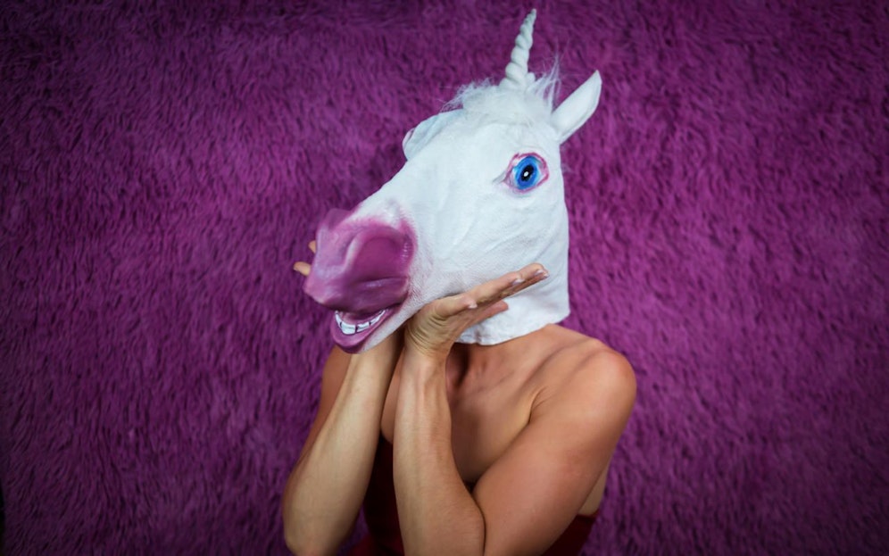 Ausgeflippte junge Frau mit Einhorn-Maske. Symbolbild