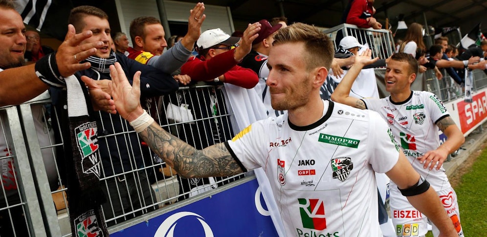 Sollbauer und Schmitz klatschen nach dem 2:0 in Hartberg mit den mitgereisten WAC-Fans ab. 