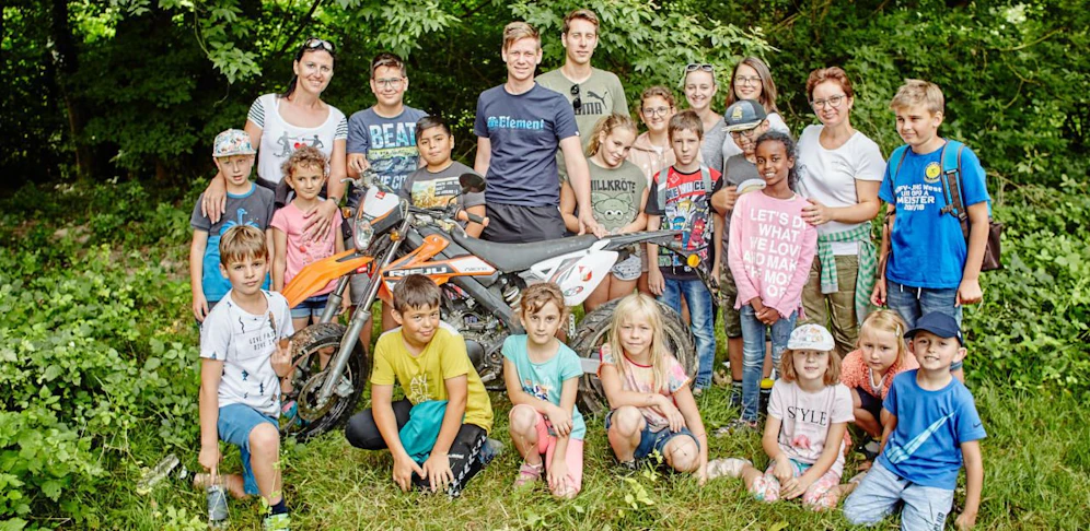 Die Kinder der Nachmittagsbetreuung posieren mit Leiterin Verena Thöni und den glücklichen Mopedbesitzern beim gefundenen Moped auf der Melker Donauinsel.