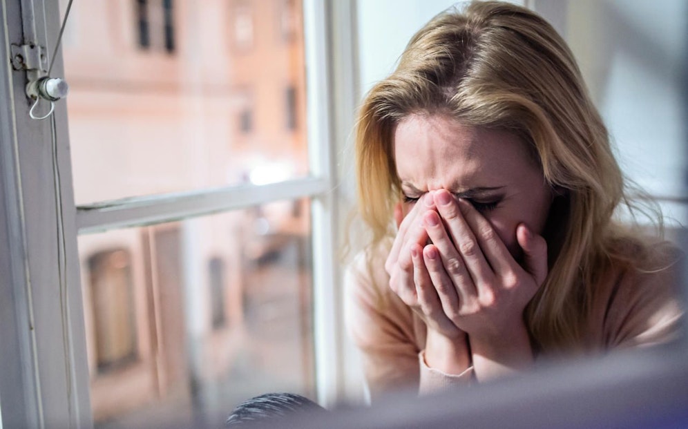 Eine Frau sitzt weinend auf der Fensterbank. Symbolfoto
