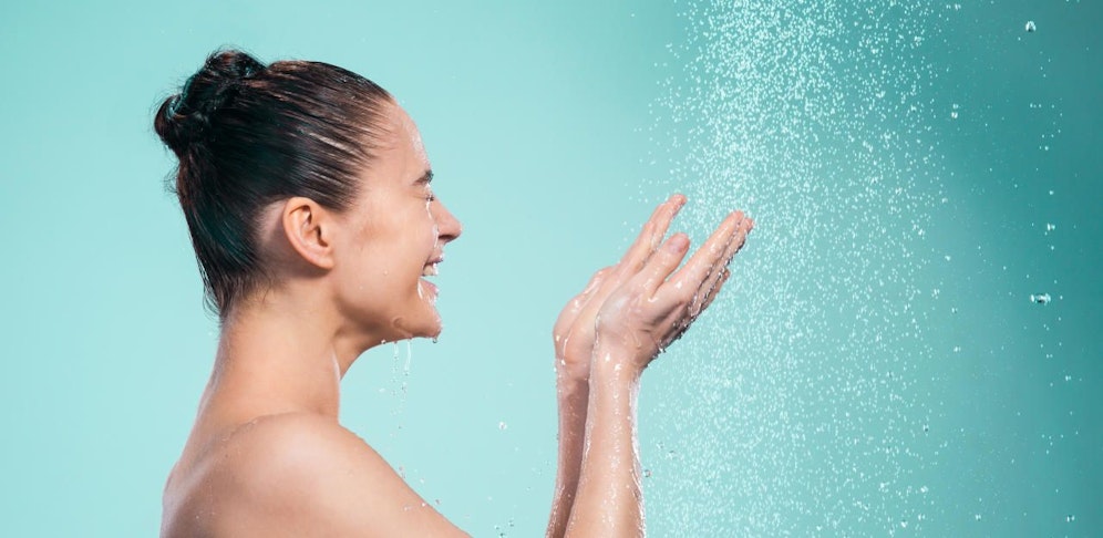 Woman enjoying the water in the shower under a water jet on blue background