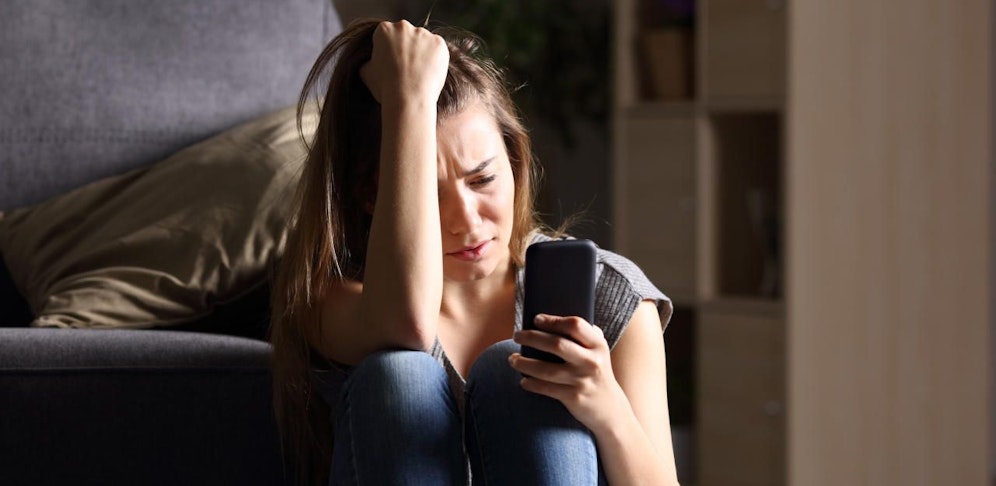 Symbolbild einer verzweifelten Frau mit Handy.