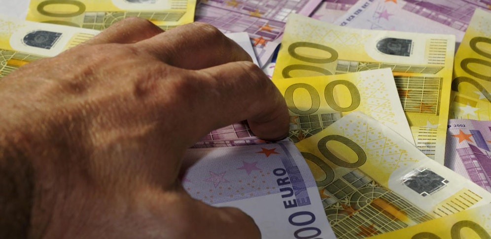 Eine Hand greift nach Euro-Scheinen. Symbolfoto.