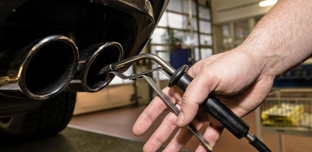 Ein Techniker des deutschen TÜV überprüft die Abgase eines Autos mit einer Messsonde.