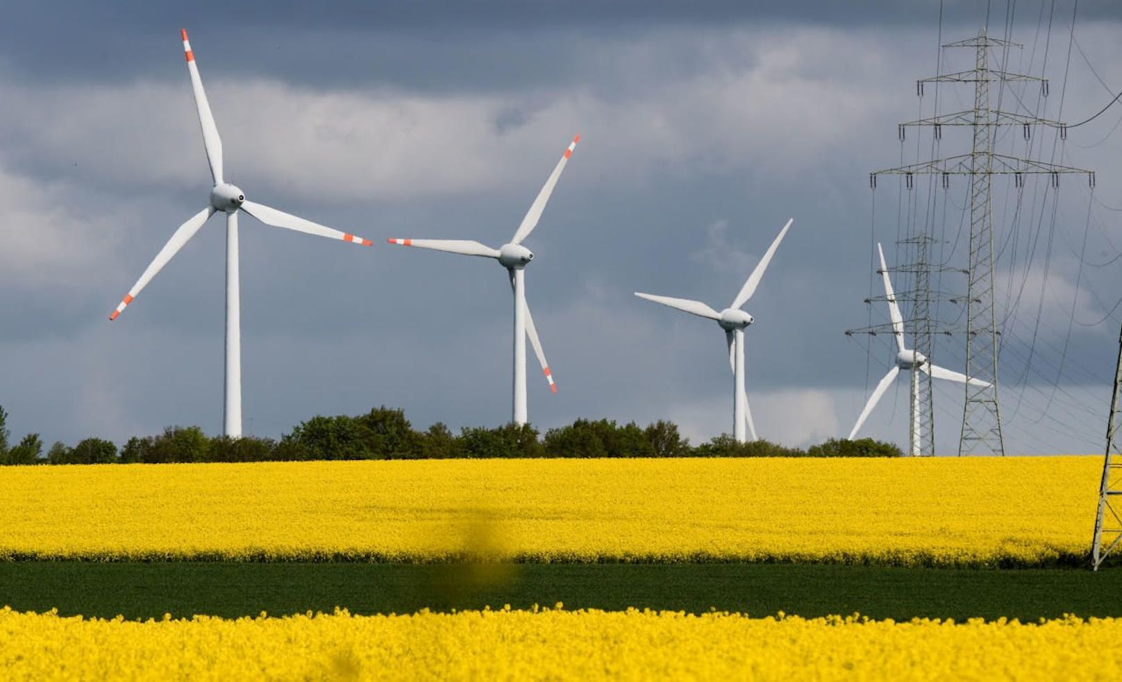 Eine Hochspannungsleitung und Windkrafträder vor einem Rapsfeld. Aufgenommen am 3. Mai 2019. 