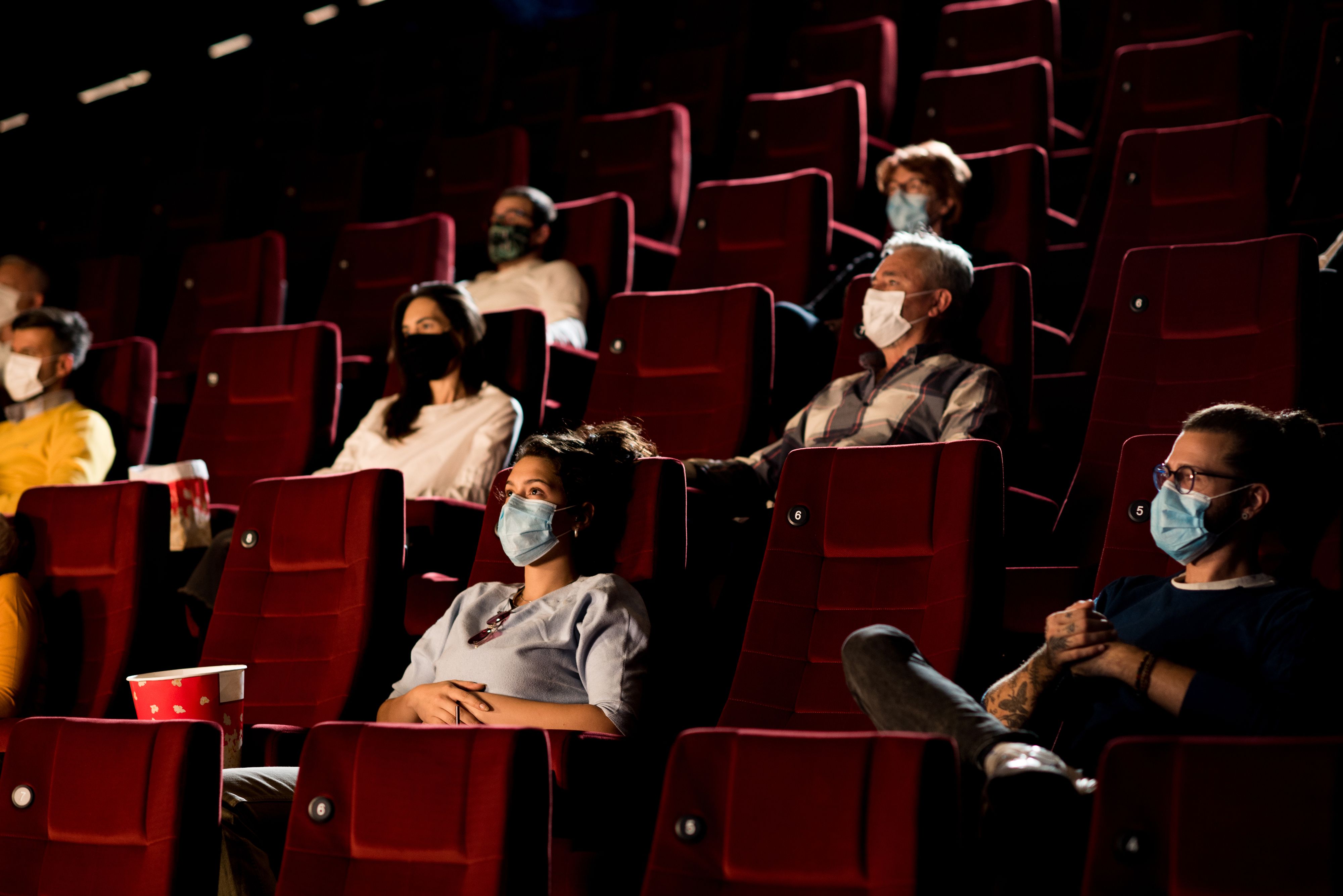 Audience at the cinema wearing protective face masks and sitting on a distance while watching the movie.
