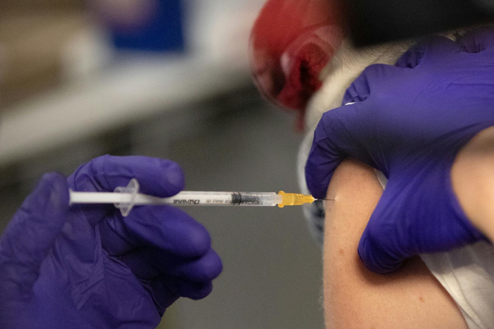 Eine Mitarbeiterin mit blauen Handschuhen impft eine Frau in einer Corona-Impfstraße. (Symbolbild)