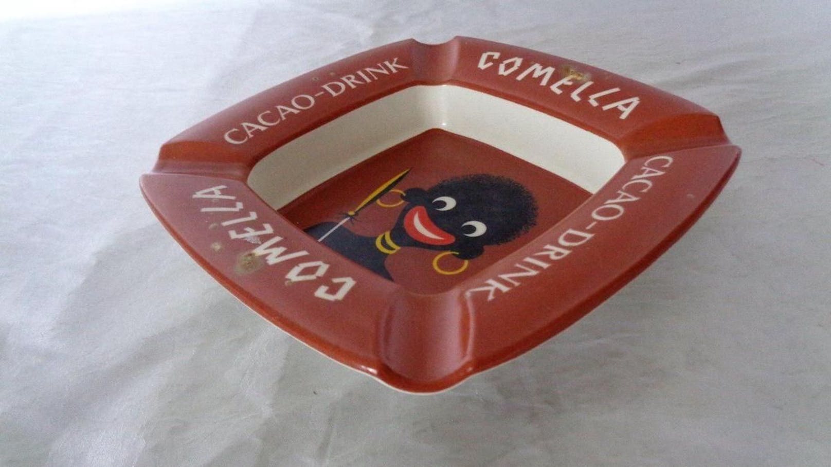 Denn das alte Comella-Logo bediente sich afrikanischer Stereotype: eine schwarze Figur mit roten Lippen, großen Ohrringen, Halsreifen und Speer in der Hand.
