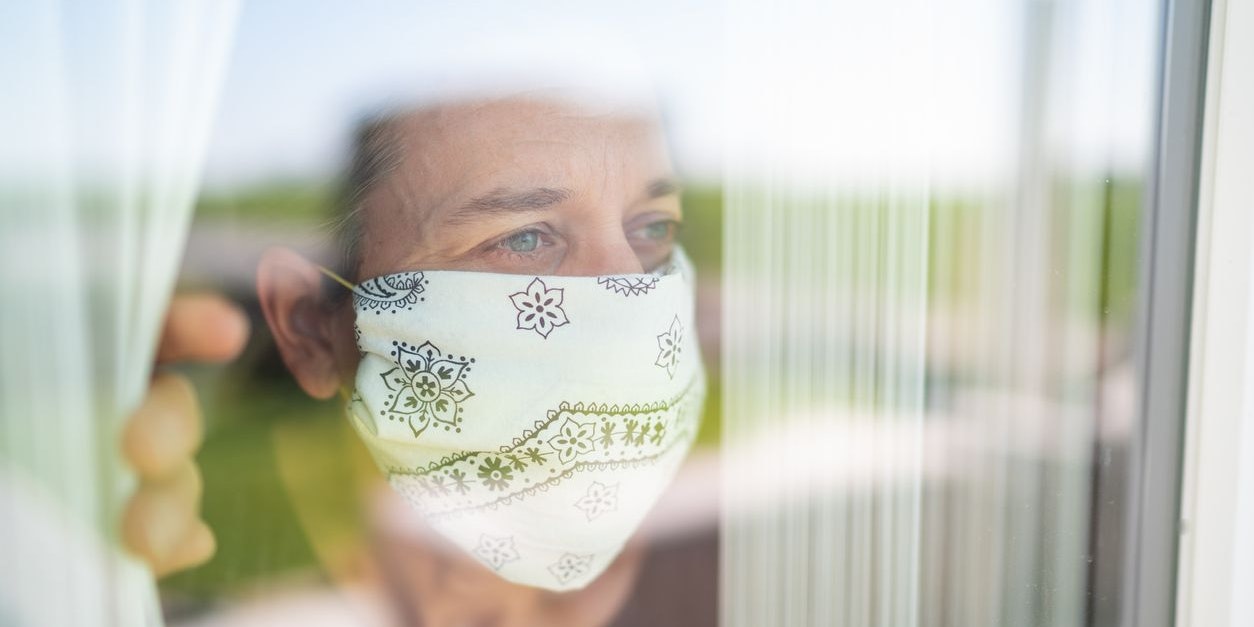 face of woman with selfmade mouth nose mask looking out of the window during coronavirus curfew quarantine hoping for better times to come, view from outside