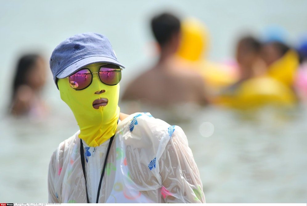 Strandbesucherin mit Facekini als Sonnenschutz in Qingdao / China.