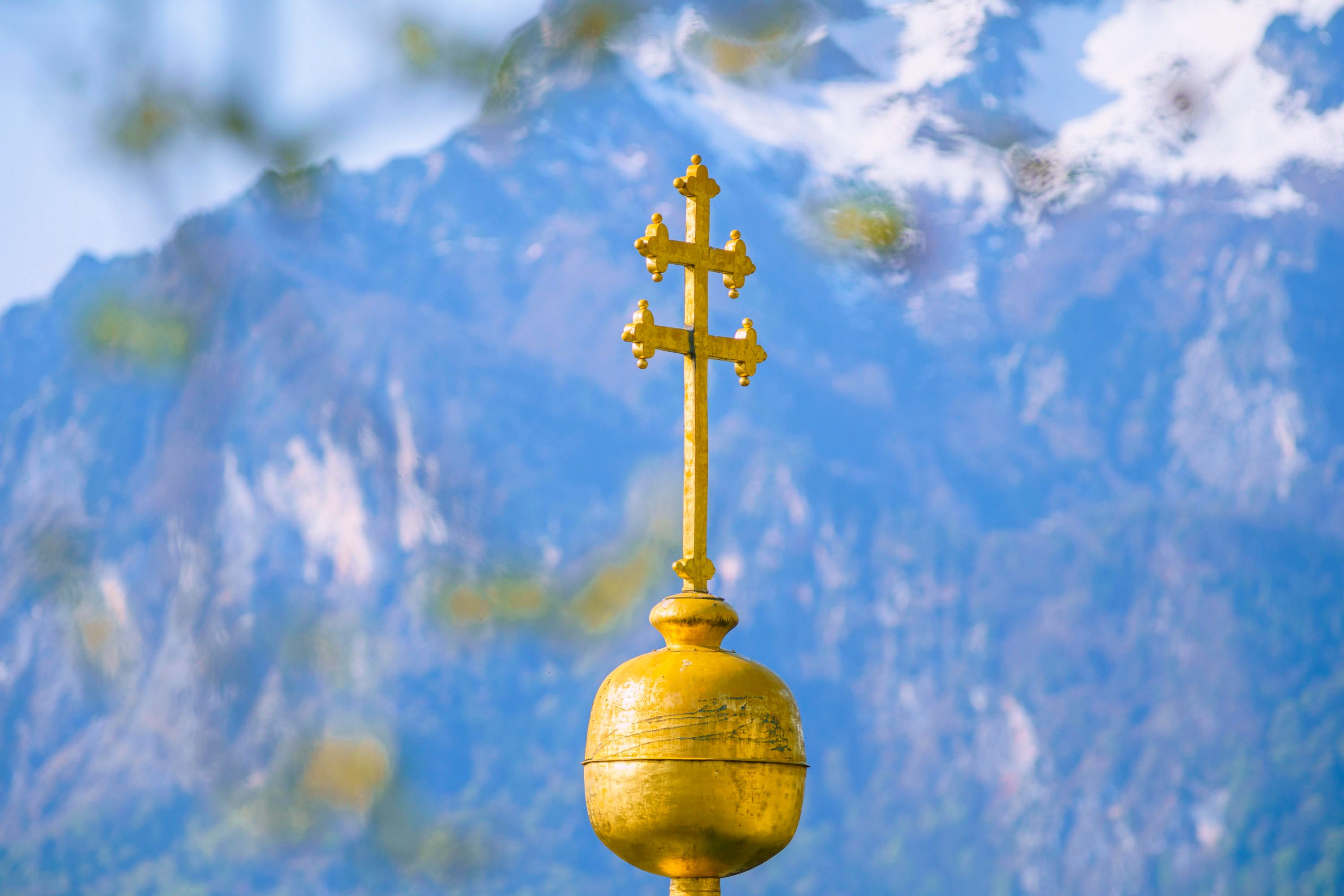 Download von www.picturedesk.com am 05.08.2021 (11:03).  Das Kreuz auf der Pfarrkirche St. Erhard im Ortsteil Nonntal in der Stadt Salzburg vor den noch schneebedeckten Bergen der Berchtesgadener Alpen während die Platane im Vordergrund schon erste Blätter austreibt - 20200417_PD3822 - Rechteinfo: Rights Managed (RM)
