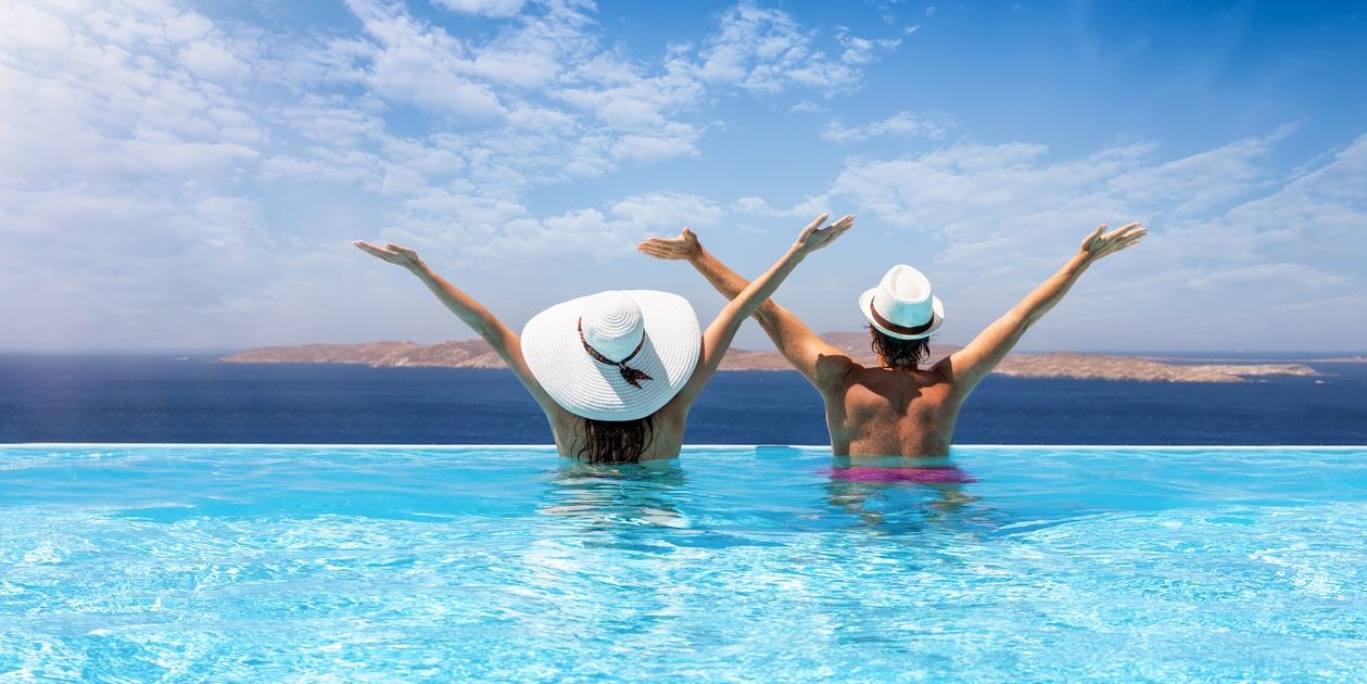Happy traveler couple with sunhats in a infinity swimming pool enjoys the view to the Mediterranean sea