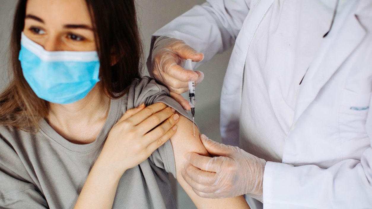 Young woman with face mask getting vaccinated, coronavirus, covid-19 and vaccination concept. Closeup of a nervous woman and her doctor wearing face masks and getting a vaccine shot in a doctor's office