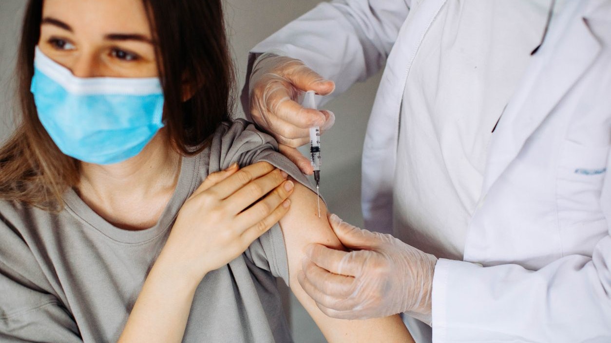 Young woman with face mask getting vaccinated, coronavirus, covid-19 and vaccination concept. Closeup of a nervous woman and her doctor wearing face masks and getting a vaccine shot in a doctor's office