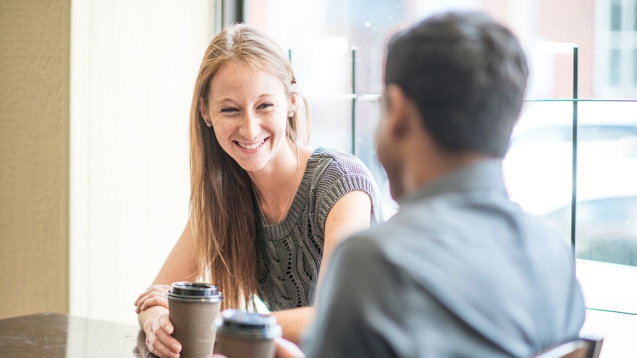 A couple is on their first date at a cafe. They are talking and are getting a cup of coffee.