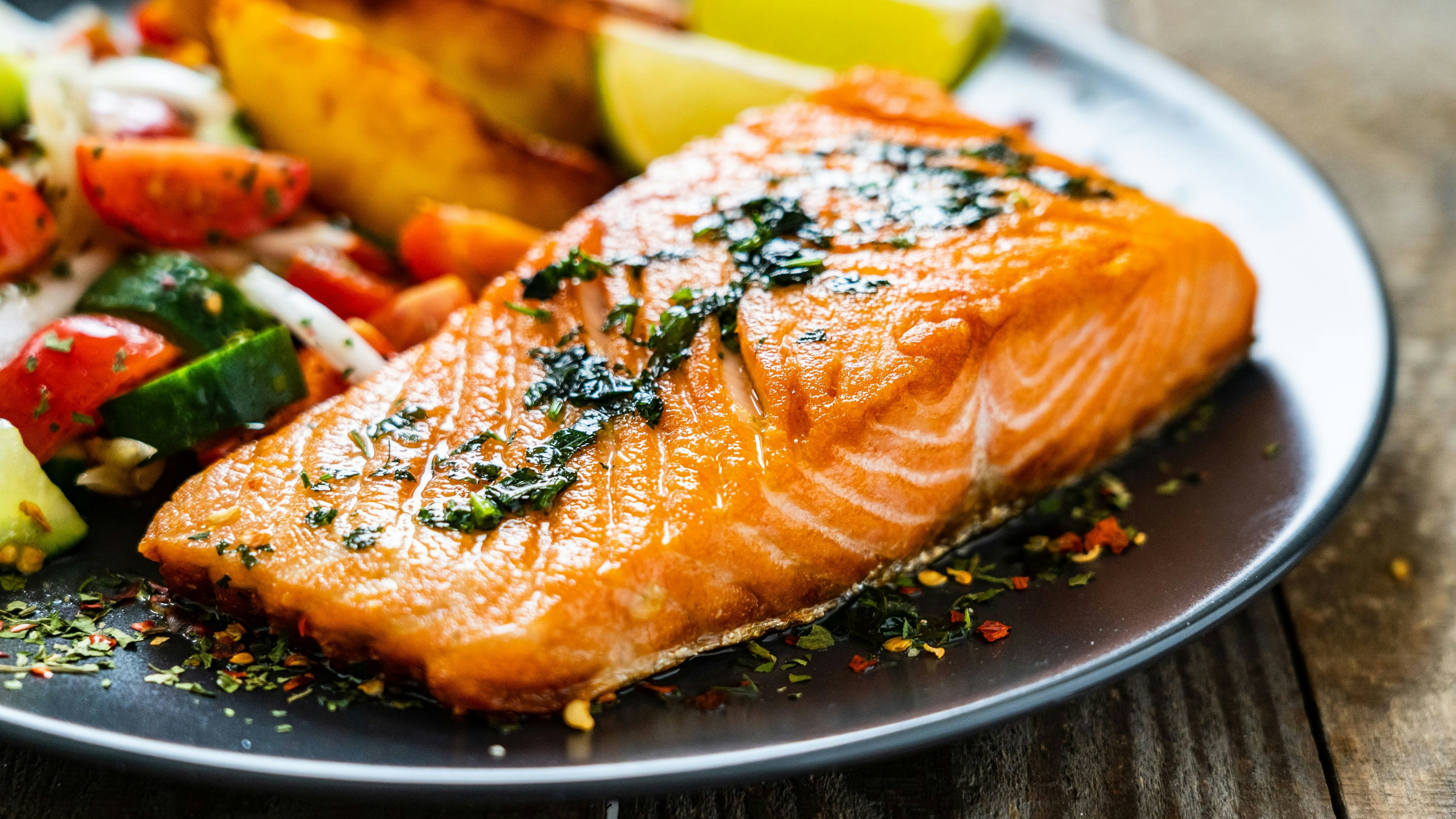 Fried salmon steaks, fried potatoes and fresh vegetables on wooden table