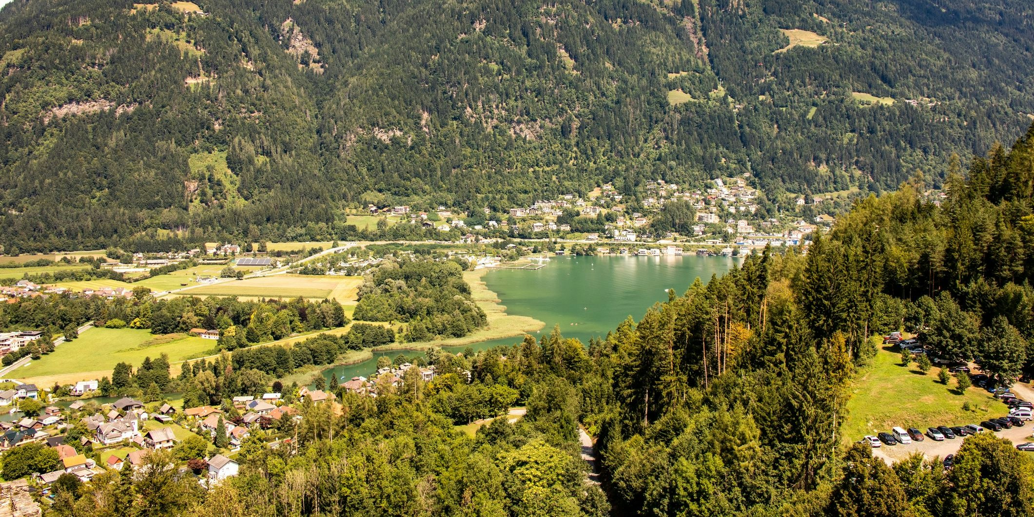 Der Ossiacher See von Villach aus gesehen, im Vordergrund hinter den Bäumen die Seeuferstraße.