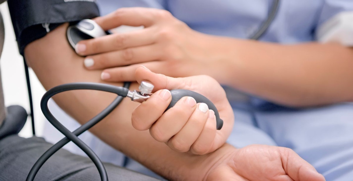 Close-up of nurse checking male patient's blood pressure with blood pressure gauge.