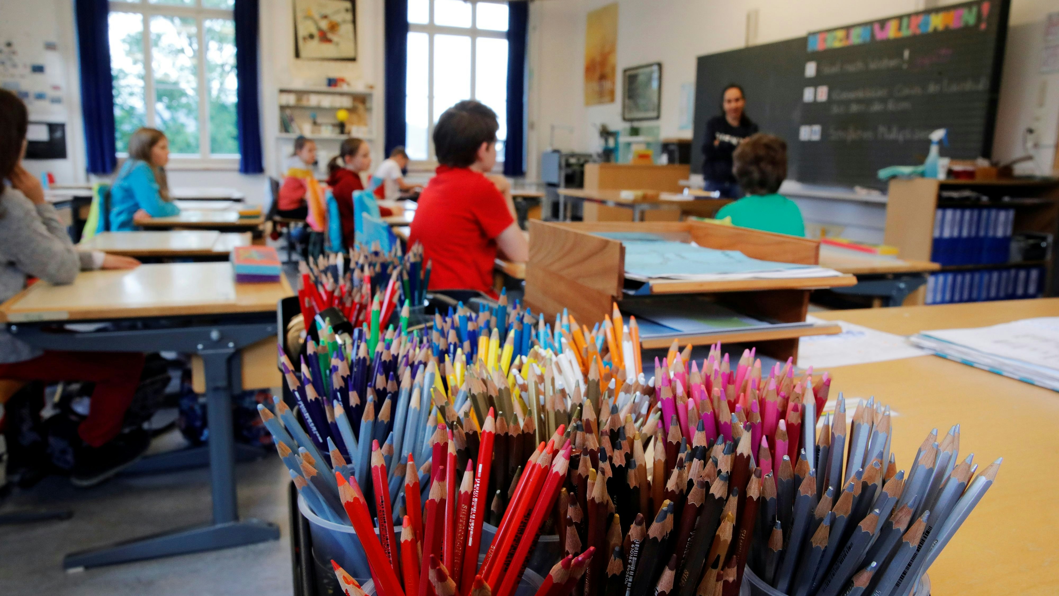 Colored pencils are seen in front as teacher Simona Fischer talks to pupils in a classroom at the Schule Hutten primary school during the first day back to school as Switzerland eases the lockdown measures during the coronavirus disease (COVID-19) outbreak in Zurich, Switzerland May 11, 2020. REUTERS/Arnd Wiegmann