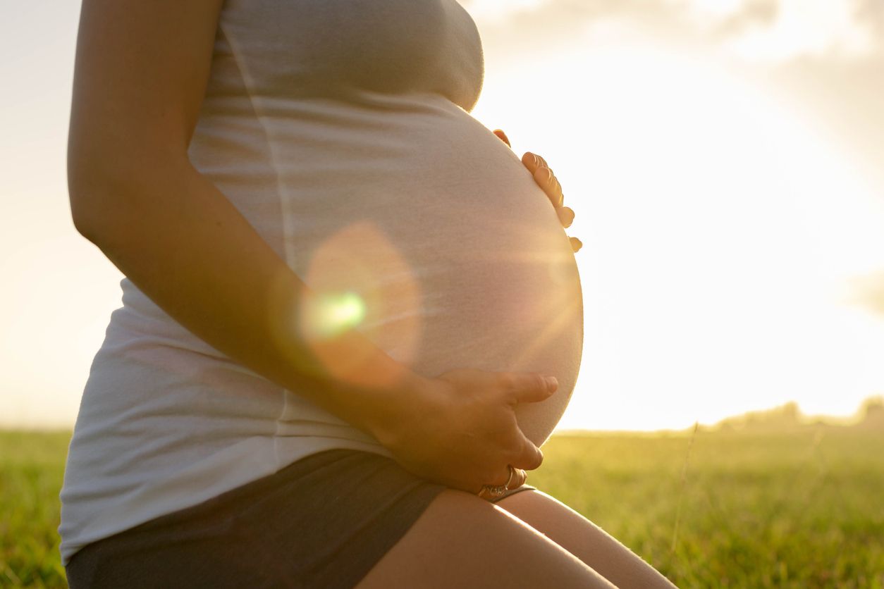 A mom holding her pregnant stomach with the sun shining on it.