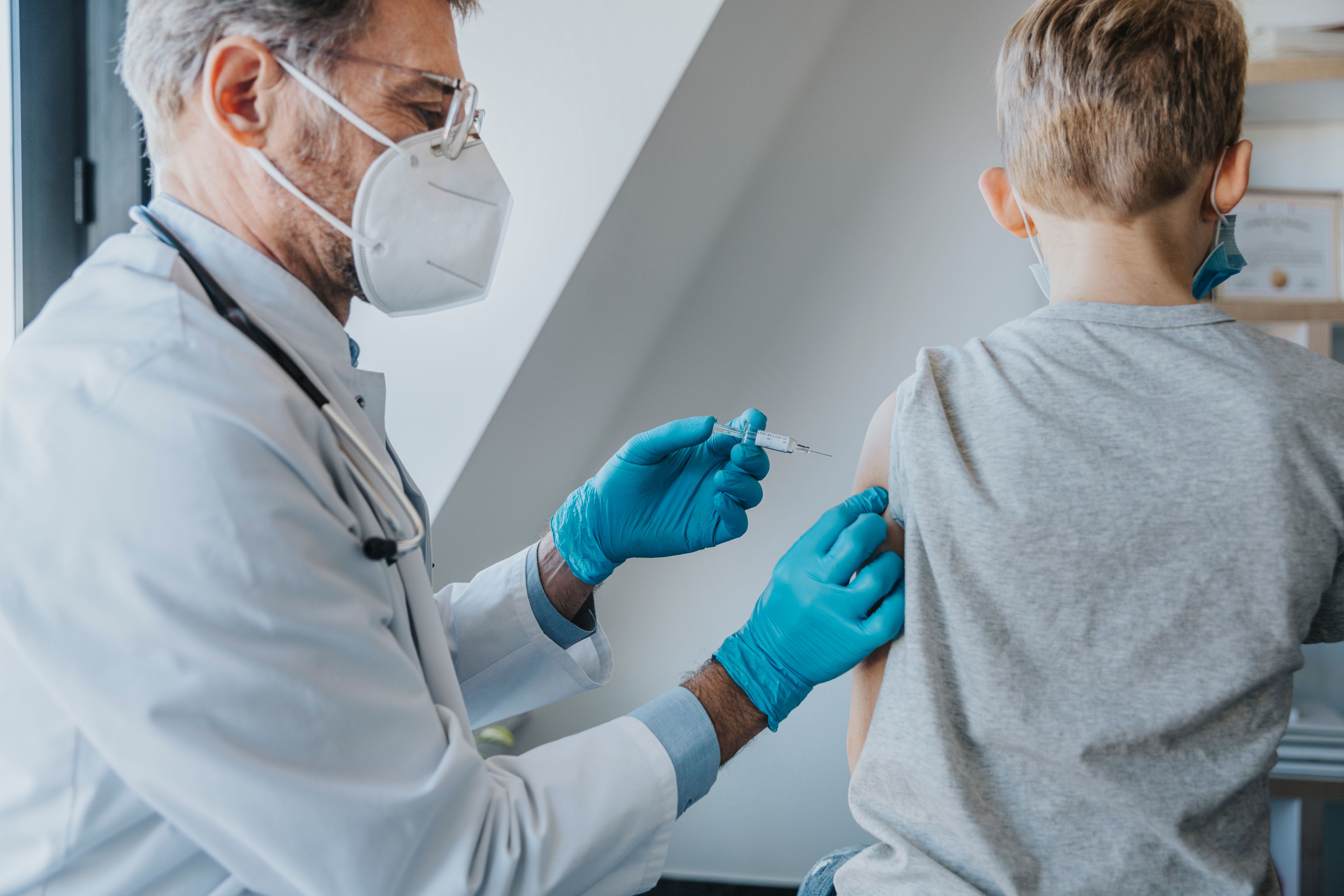 Download von www.picturedesk.com am 03.09.2021 (11:17).  Doctor wearing protective face mask giving COVID-19 vaccine to boy while standing at clinic - 20210227_PD16712 - Rechteinfo: Royalty Free (RF) Model Released