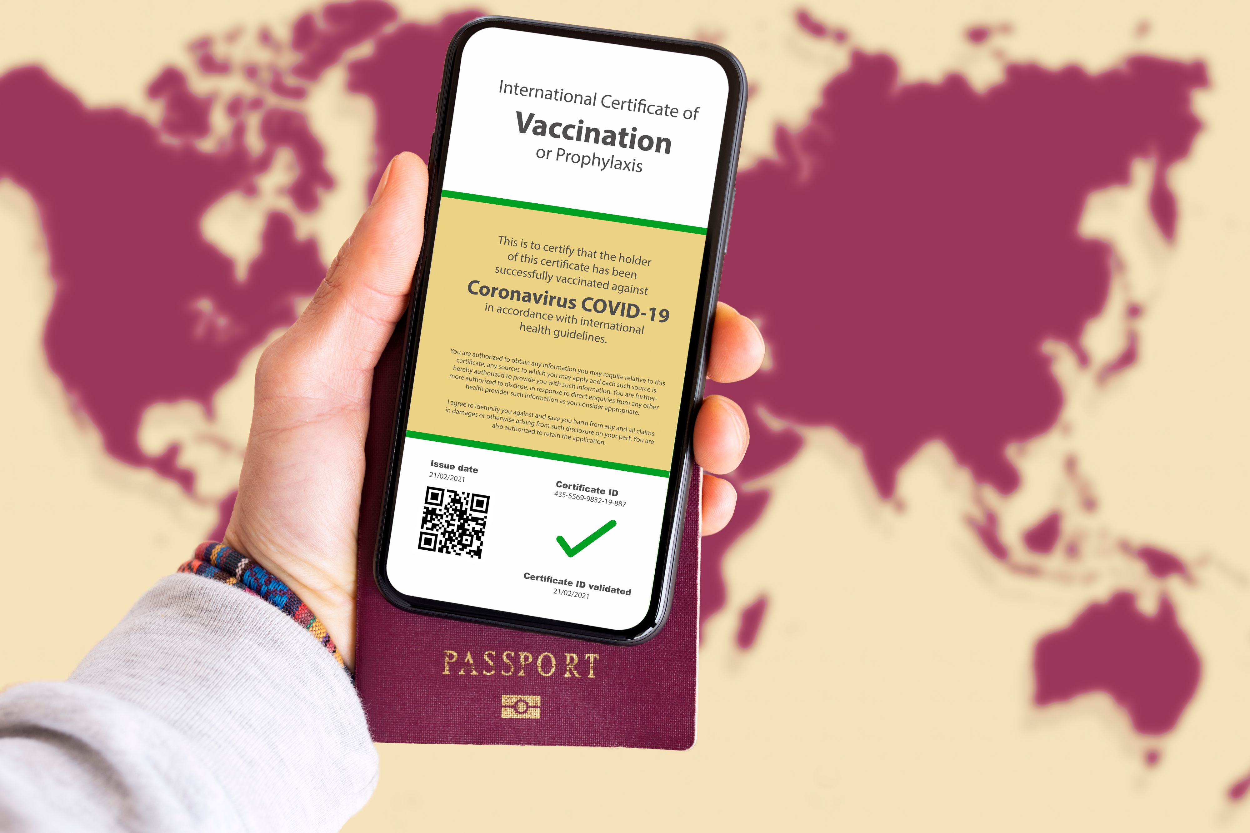 Human hand holding a smart phone with a certificate of vaccination against Coronavirus, COVID-19 with blurred World Map in the background. Travel concept during the Covid-19 pandemic.