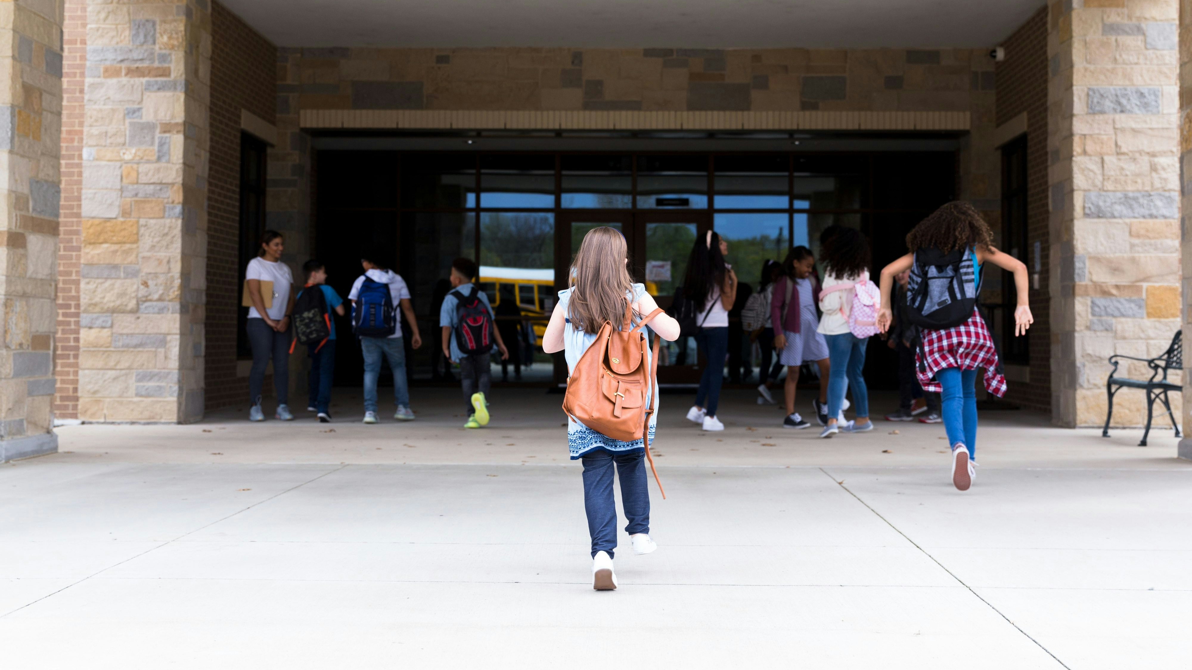 Rear view of elementary schoolgirl walking into the school building