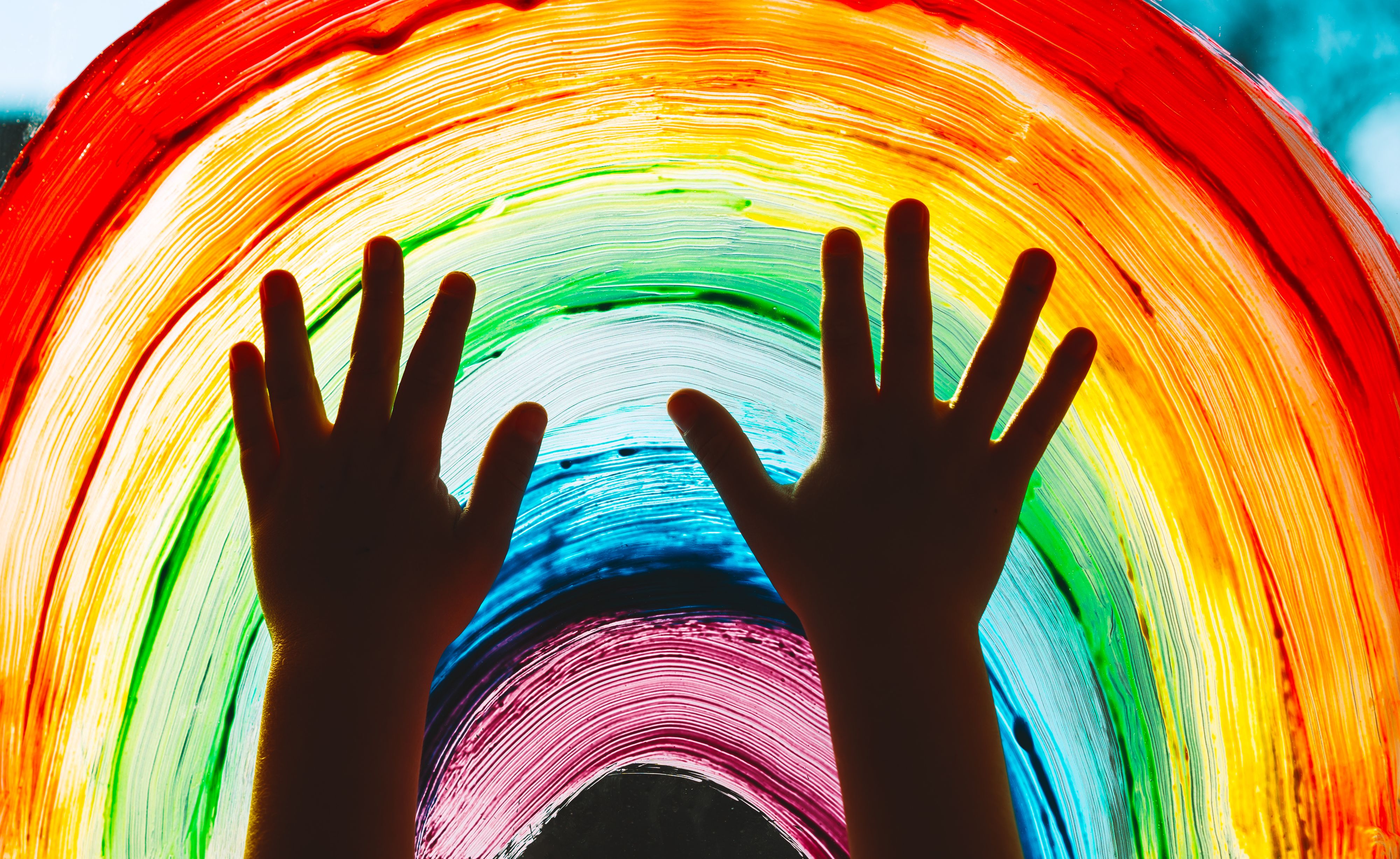 Close-up photo of child's hands touch painting rainbow on window. Family life background. Image of kids leisure at home, childcare, safety joy symbol.