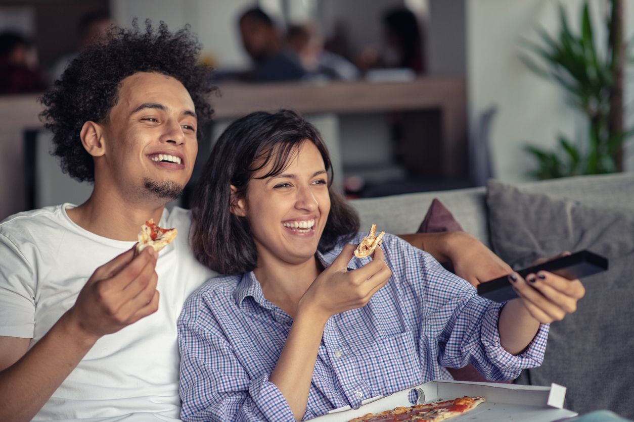 Happy couple watching tv while eating pizza. Shallow depth of field, focus on the man.